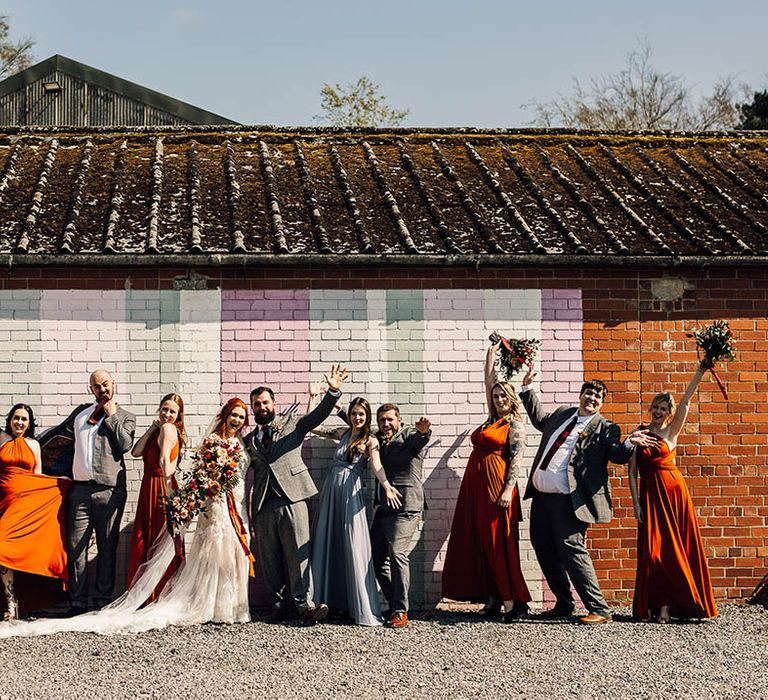 Wedding party stands together in front of pastel painted colourful wall 