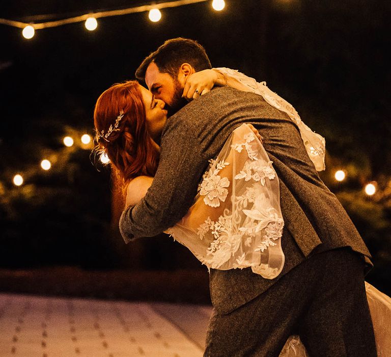 Groom sweeps the bride low for a kiss under pretty festoon lighting 