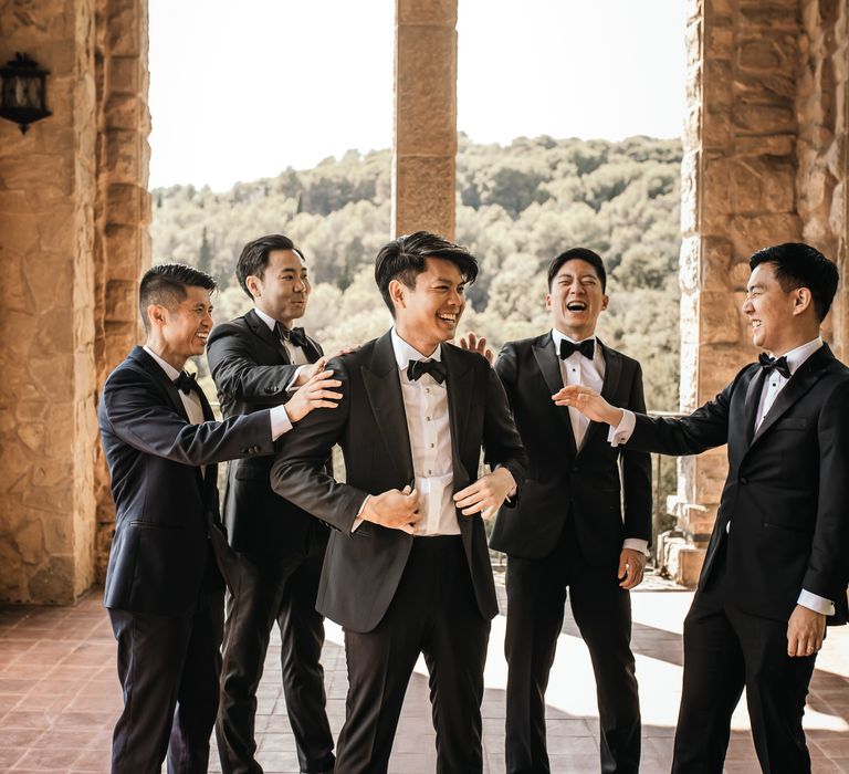 Groom stands with his groomsmen in the La Baronia wedding venue all wearing black-tie 