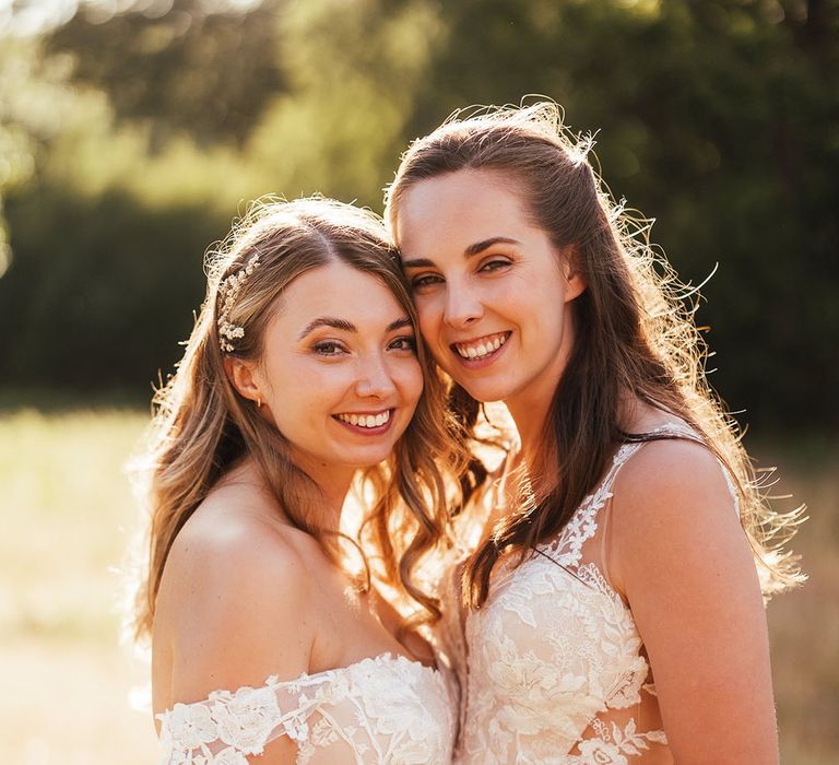 Brides smile at the camera during golden hour in lace wedding dresses for their woodland wedding 