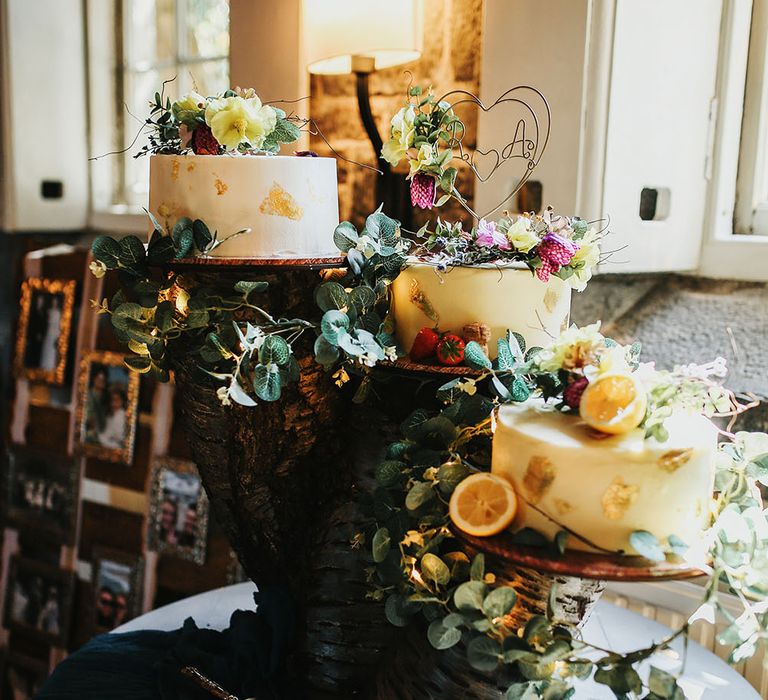 DIY tree trunk cake stand finished with three white frosted wedding cakes and floral decor 