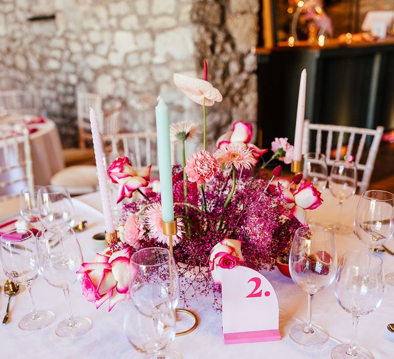 Bright pink floral centrepiece for modern tablescape complete with pink table numbers and pastel candles in gold candle holders 