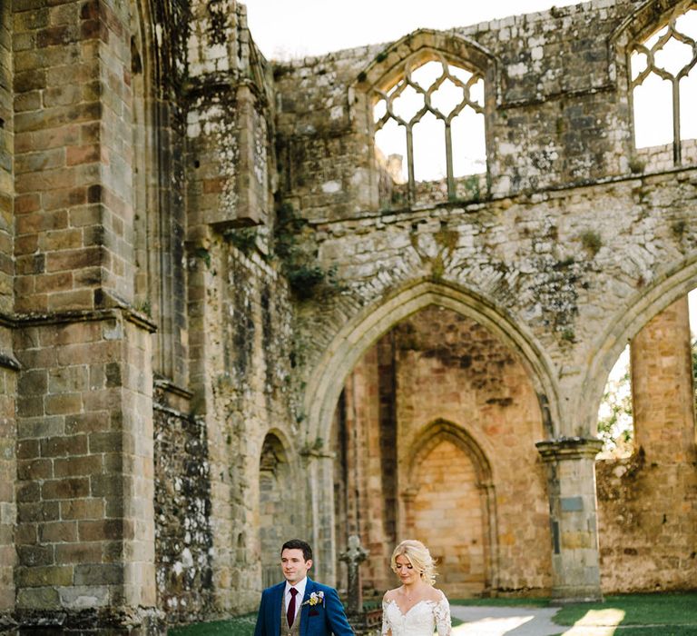 Bride & groom walk through castle ruins during couples portraits as the sun begins to set on their wedding day