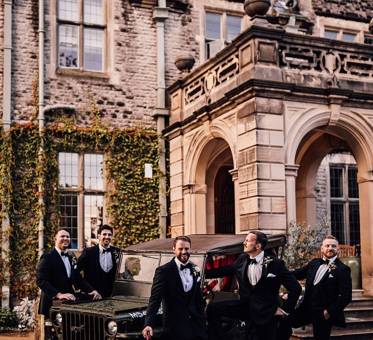 Groomsmen in black tie all stand together around the Jeep wedding car transport 