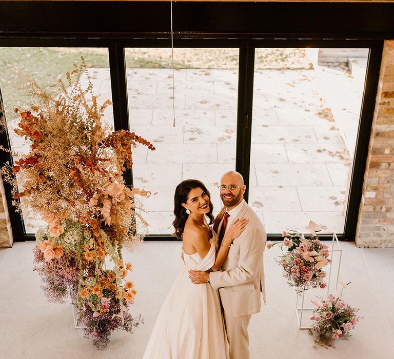 Bride and groom embrace at the altar looking up at the camera with the rust and lavender wedding flowers 