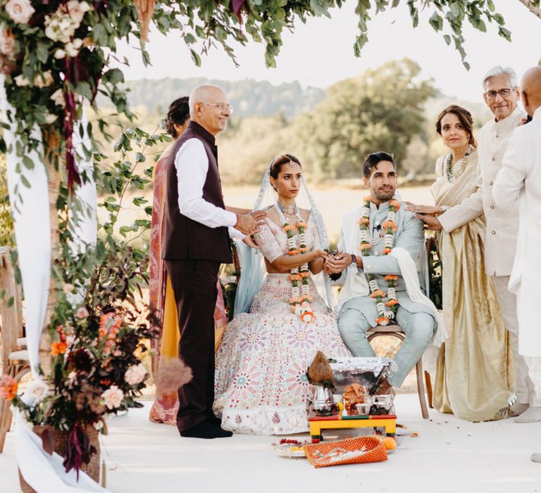 Indian bride & groom during traditional wedding ceremony outdoors surrounded by family 