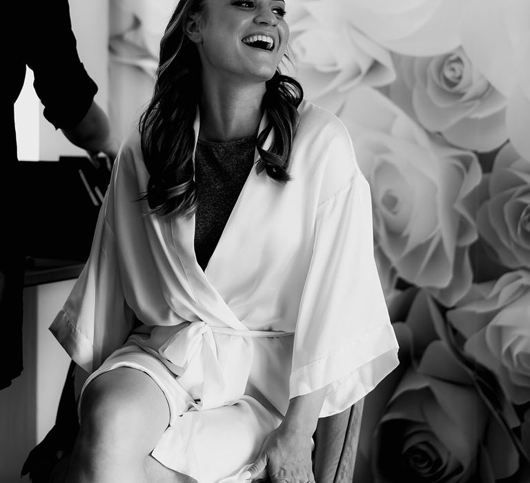 Bride sits in a white satin robe as she gets her makeup done for the rustic wedding day 