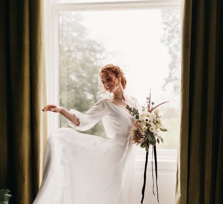 Bride dancing, showing off her full satin wedding skirt holding neutral, minimalistic floral bouquet with black crushed velvet ribbon