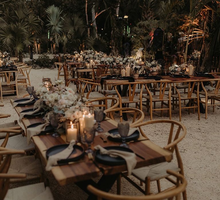 Wooden banquet tables complete with black plates and neutral toned fabric napkins alongside white pillar candles 