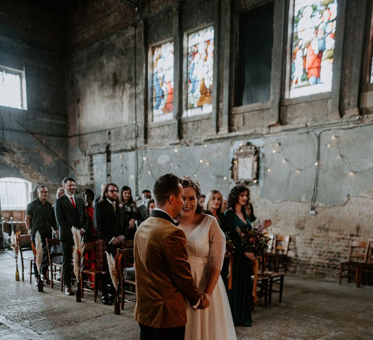 Couple holding hands and laughing at the alter in London wedding venue, The Asylum Chapel