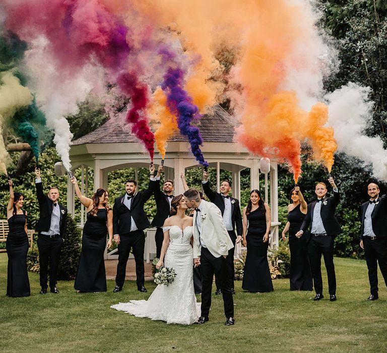 Bride and groom with their wedding party in monochrome black and white outfits let off colourful smoke bombs