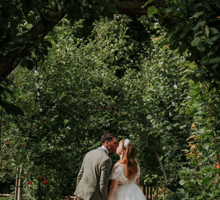 The groom in a tweed suit leans in for a kiss with the bride in a tulle wedding dress and white flower headband for their Northern Ireland wedding 