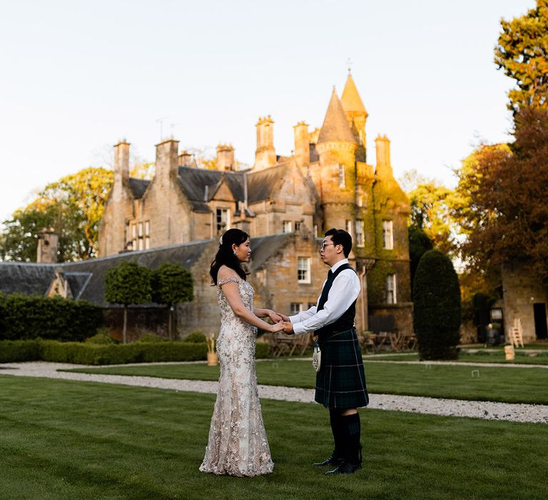 Bride in bespoke dress holds her grooms hands outdoors during golden hour