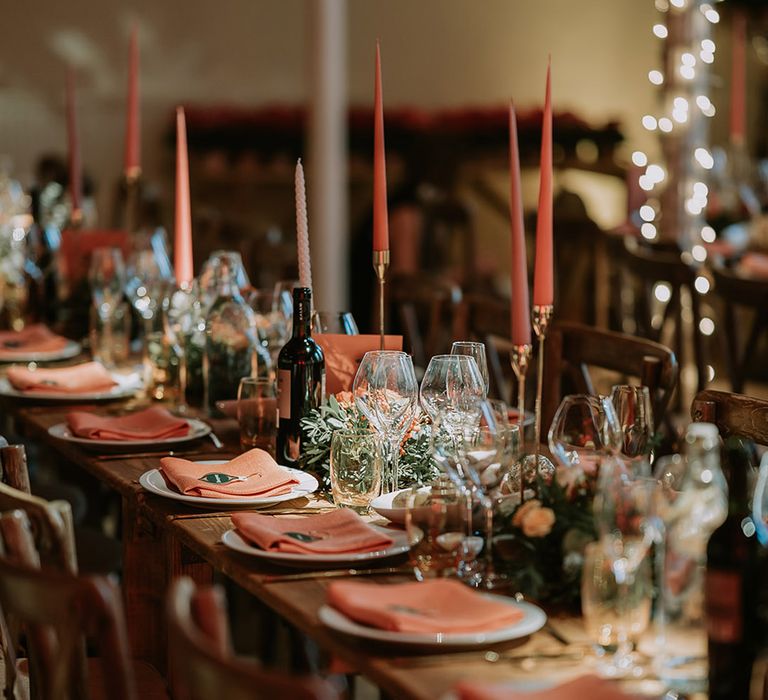 Neutral Christmas wedding tablescape with orange tapered candles, orange napkins, orange rose and foliage tablerunners and fairy lights 