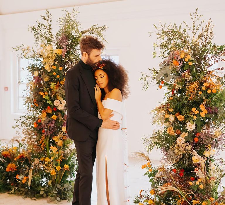 Bride and groom stand together at the altar decorated with wedding flower columns with yellow, orange, and red flowers 