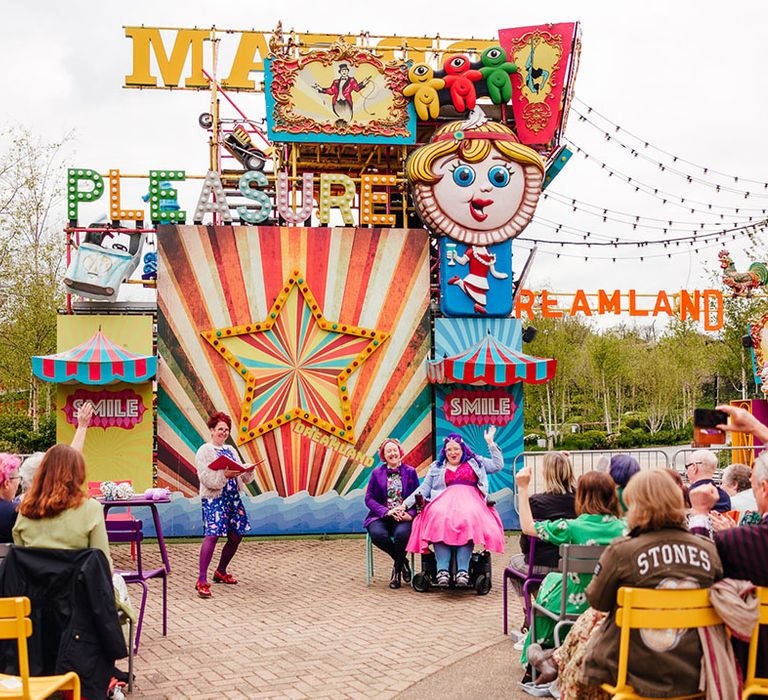 Margate Dreamland theme park wedding - brides sitting at the end of the alter in front of large colourful theme park ride 