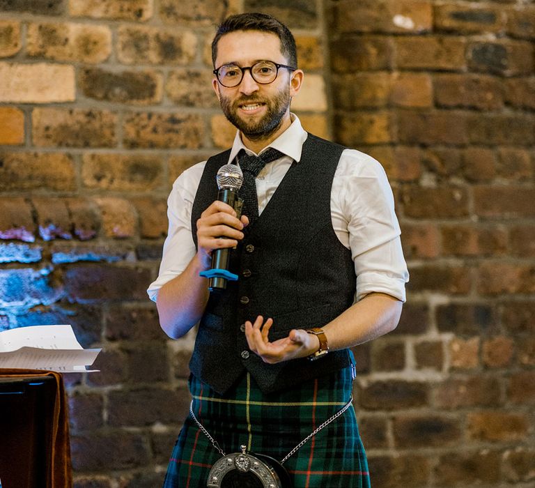 Groomsmen gives speech wearing waistcoat complete with tartan kilt 