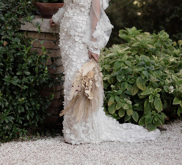 Bride wears appliqué Pronovias wedding dress with sweetheart neckline and removable sheer sleeves whilst holding pampas grass bouquet