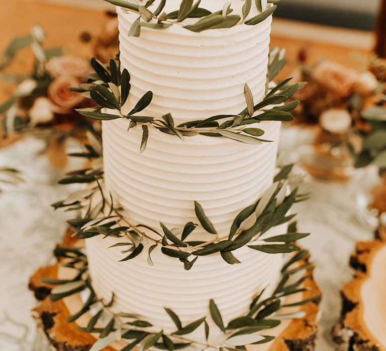 Three tier white frosted wedding cake with leaf decoration for rustic luxe wedding on a tree trunk cake stand 