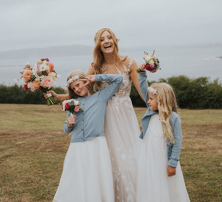 Flower girls in tulle white dresses with light blue cardigans posing with the bride in lace and tulle wedding dress with pastel wedding flower bouquets 