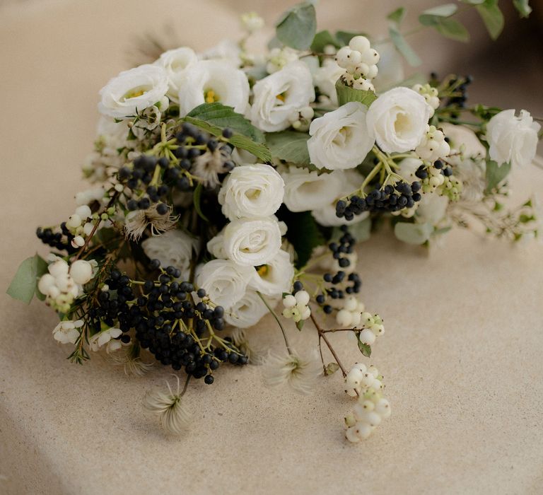 White flower bouquet featuring white roses, white berries, italian ranunculus and eucalyptus