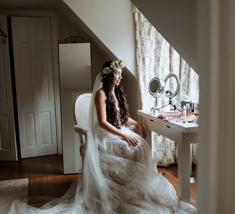 Bride in ethereal celestial wedding dress with cathedral veil sitting at vanity table before wedding 