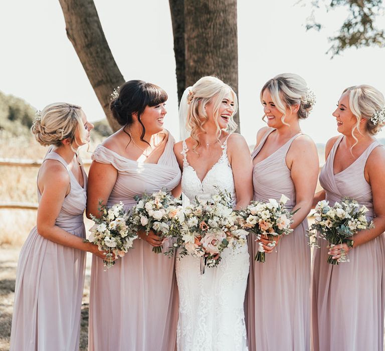 Bridesmaids in pink bridesmaid dresses with the bride in a fitted lace wedding dress with gypsophila in their hair and white bouquets 