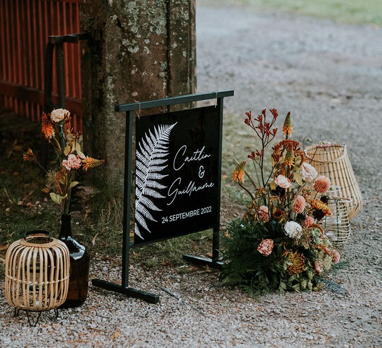 Black wedding welcome sign with leaf design, wildflowers and wicker baskets