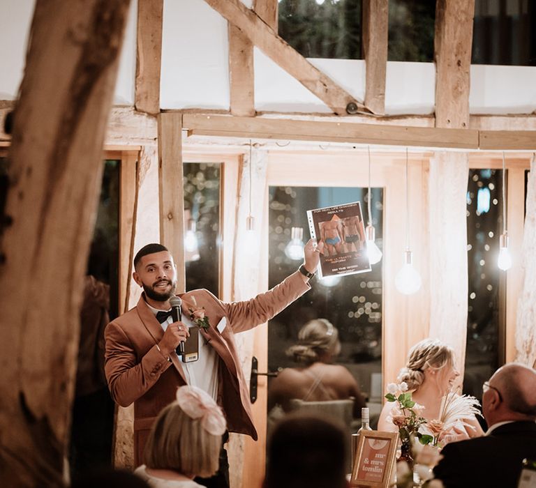 The best man in a blush pink velvet suit reads out his best man speech 