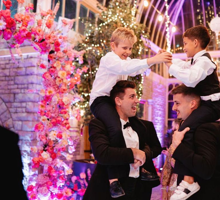 Groomsmen lift two boys on their shoulders to play at the wedding reception 