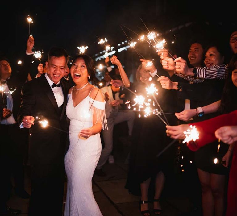 Bride in white beaded and sequined slip wedding dress and groom in classic black wedding tux doing sparkler send off at Burmese wedding at Bron Eifion