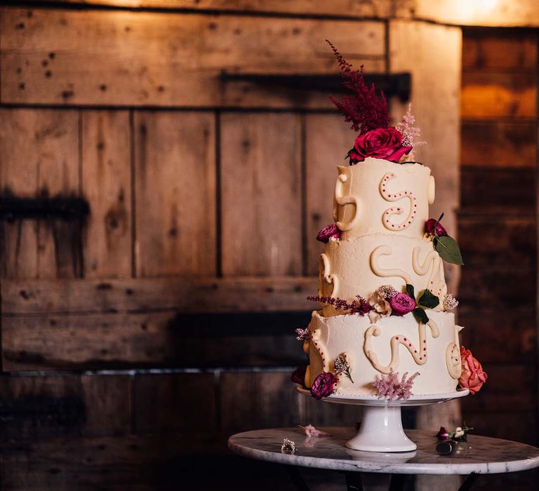 Three tier white frosted wedding cake decorated with pink flowers and squiggly icing 