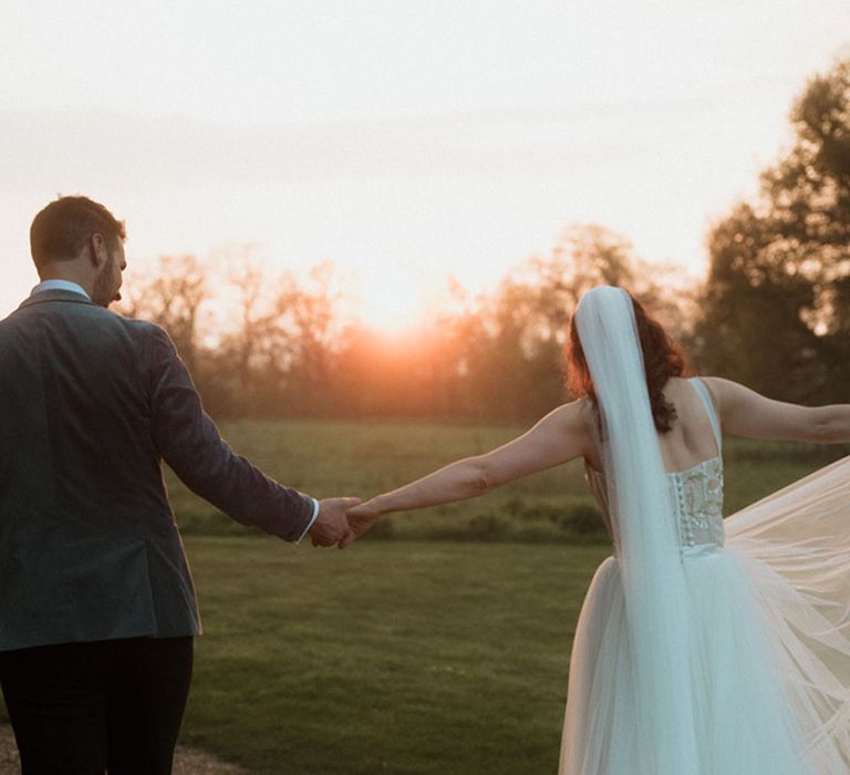 The bride and groom walk hand in hand at golden hour 