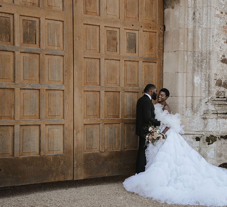 Bride in stunning tulle off the shoulder wedding gown with long train with the groom in black tuxedo 