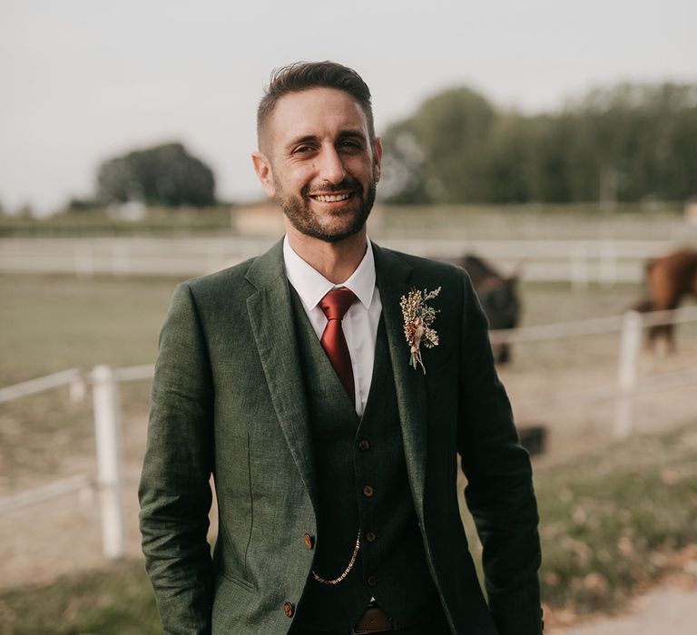 groom in three-piece wedding suit with red tie at riding school wedding 