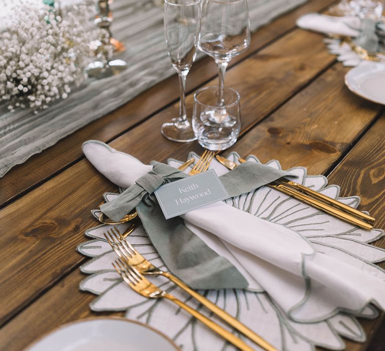 Floral place mats with gold and sage green wedding theme including gold cutlery and pastel candles and bud vases 