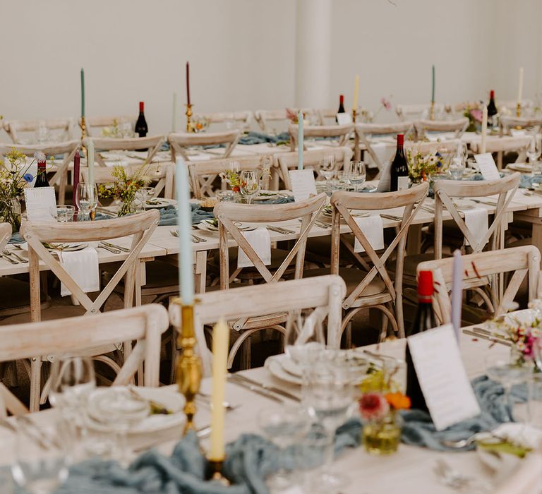 Long banquet tables decorated with dusty blue table runners and pastel wedding candles and decor 