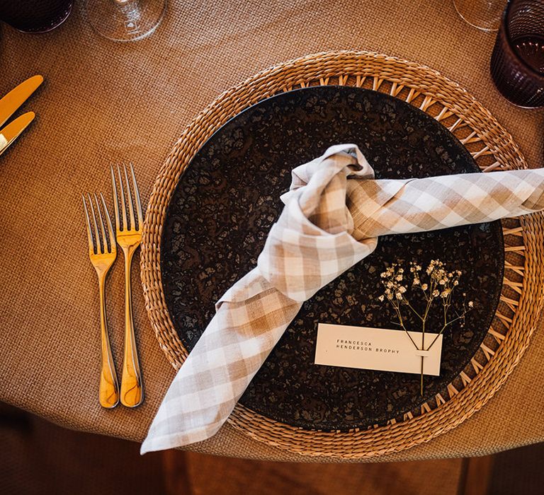 Wedding place setting with wicker place mat, black plate, checkered napkin, place name card at tipi wedding 