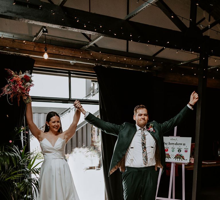 Bride in strapless wedding dress with stylish belt from Suzanne Neville with groom in dark green suit enter their wedding reception 