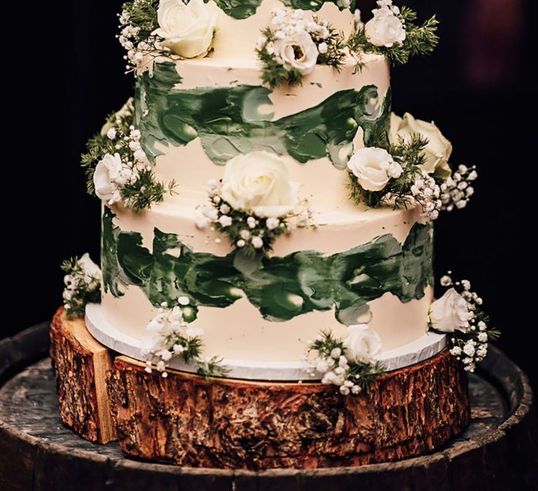 Three tier white iced wedding cake with green icing, white roses and gypsophila, polaroid cake topper on wood slice cake stand 