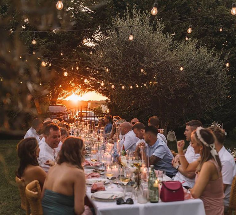 Outdoor al fresco wedding breakfast at Croatia wedding with guests eating food at sunset 