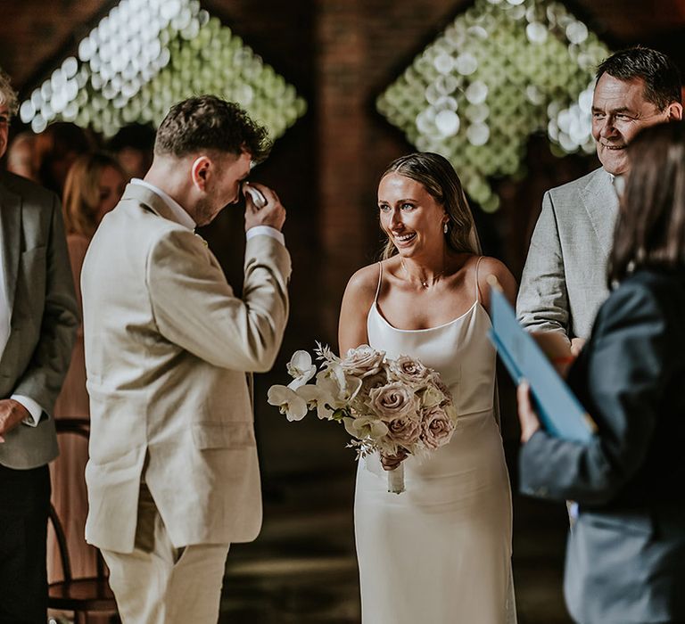 The groom wipes tears away as he sees the bride for the first time in her wedding dress 