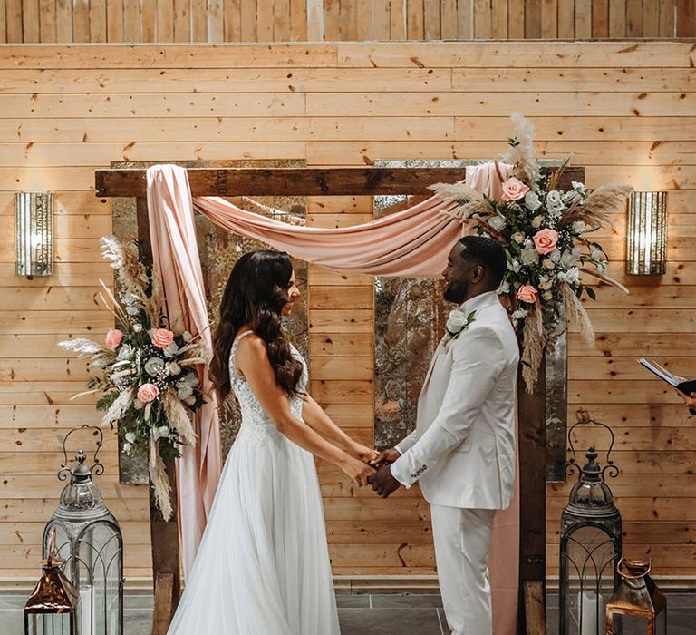 Boho luxe theme wedding with pink roses and pamaps grass flower arrangements with bride and groom at the wooden altar 