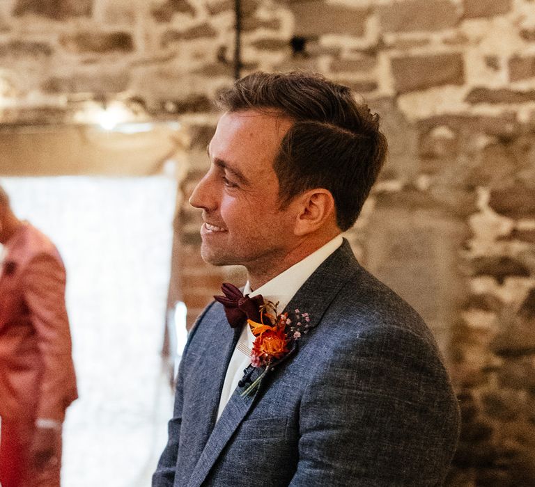 Groom wearing navy wedding suit with orange flower buttonhole 