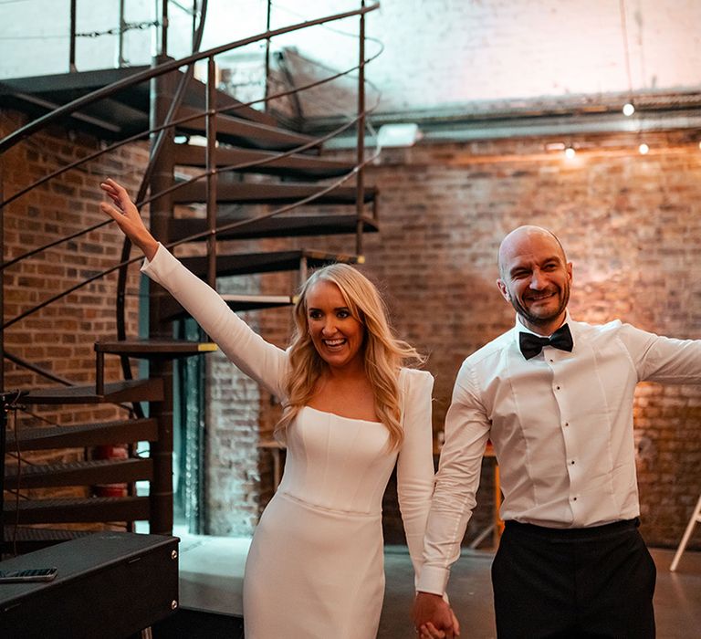 Bride wearing long sleeve Suzanne Neville wedding dress with groom in black tux entering their wedding breakfast 