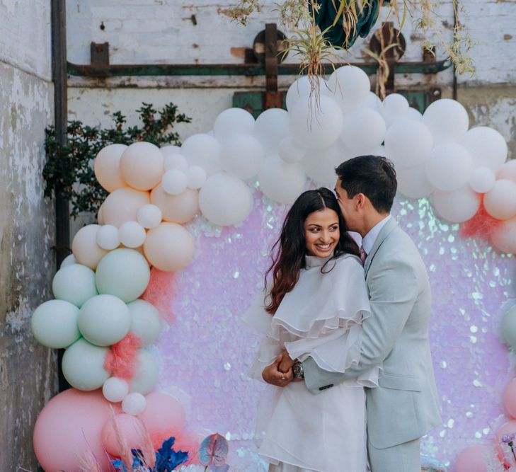 Groom in pale green suit embracing his bride in short wedding dress at holographic pastel festival wedding 