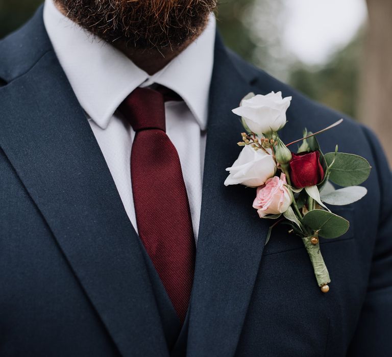 Groom in burgundy tie with white and burgundy buttonhole