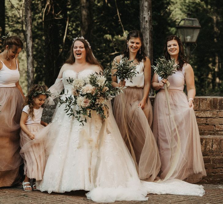 Bridesmaids play with tulle skirts while bride holds olive bouquet