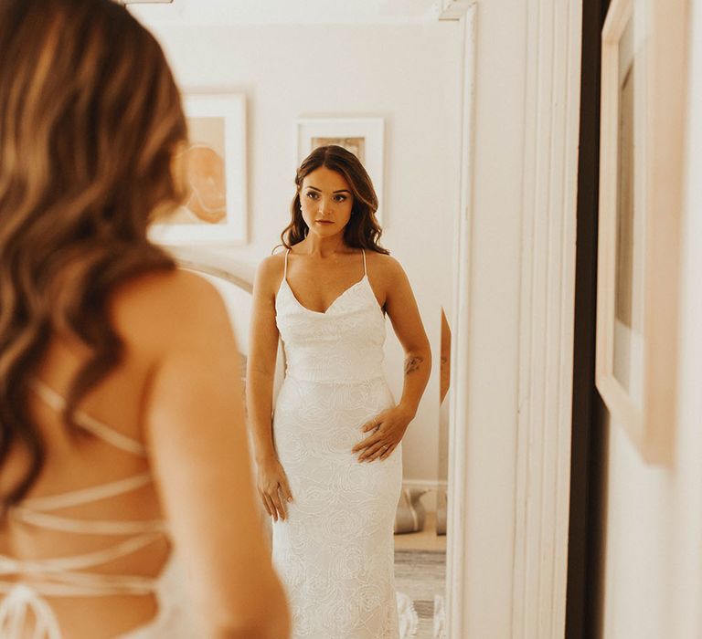 Bride looks at herself in a mirror in Grace Loves Lace backless cowl neck wedding dress