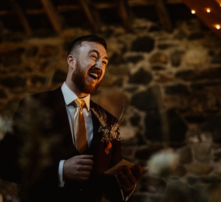 Groomsman in burgundy Marc Darcy suit laughing at wedding reception